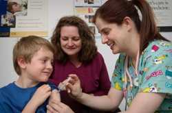 Photo of a nurse giving a vaccine to a pre-teen boy while his mother looks on.