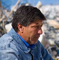 Man sitting alone in front of wreckage from a disaster.
