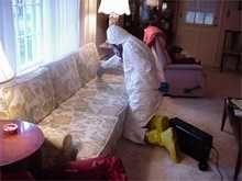 Worker in a hazmat suit test for the existence of anthrax in a couch.