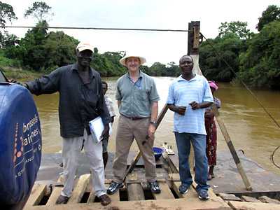 Dan Martin (center) crosses a river in Sierra Leone on a human-powered ferry with colleagues Mohamed Okala Sankoh and James Fornah. One Land Cruiser, one motorcycle, and about a dozen people were pulled across this river.