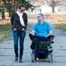 Man in an electric wheelchair strolling in a park with a friend