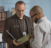 A man in glasses consults a folder with a doctor.