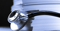photo of a stack of papers with a stethoscope draped over the stack.