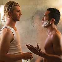 Photo of two men talking in front of a steamy bathroom mirror. One man is shirtless with shaving cream on his face.