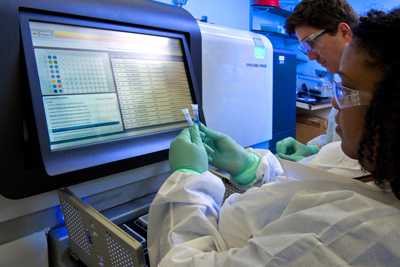 	Two lab scientists preparing vials for sequencing using a large machine