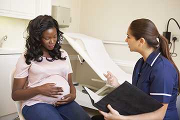 image of a pregnant woman holding her belly while talking to a physician