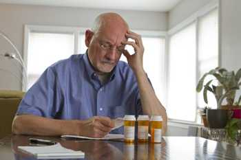 Photo of a worried man with bottles of prescription medicines