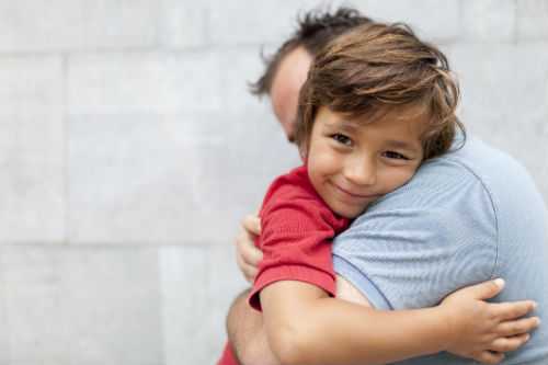 Photo of boy hugging his father around his neck