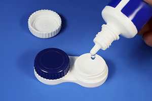 	a multipurpose solution bottle being used to clean contacts that are sitting in a storage case.
