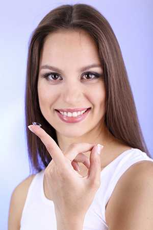 	woman holding contact lens on a fingertip smiling