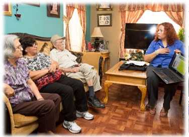 A CHW speaking to some elderly people sitting on a sofa.