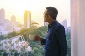 	Asian man holding cup of tea and looking out a window