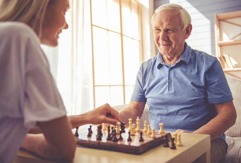 Senior man playing chess with younger woman