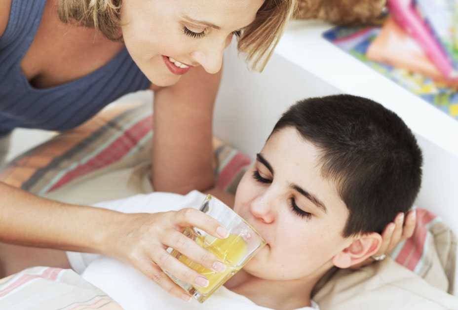 Mother giving orange juice to sick son