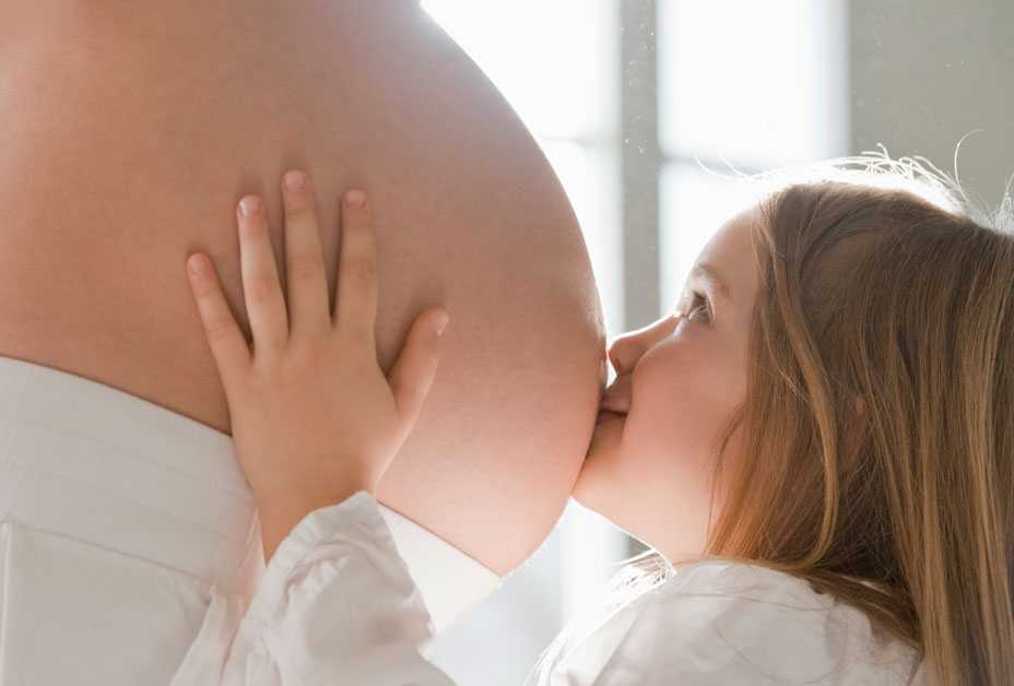 Young girl kissing pregnant mother's belly
