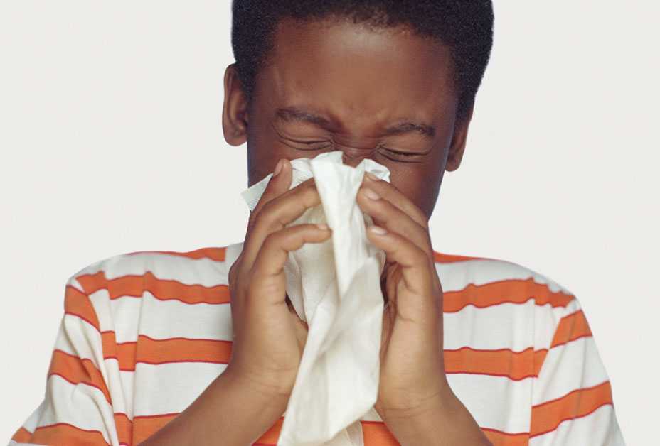 Boy sneezing into tissue