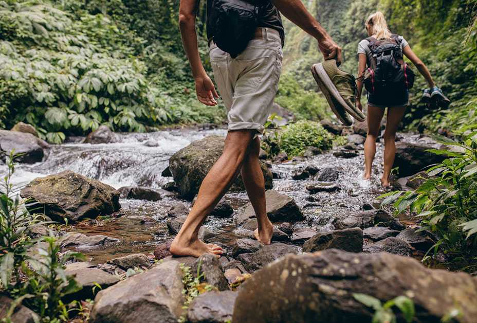 Couple hiking barefoot through stream
