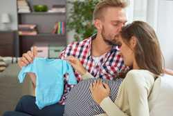Man holding baby clothes and kissing pregnant woman