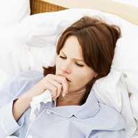 What to do if you get sick with the flu. Photo of woman in bed coughing.
