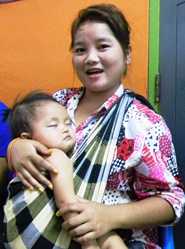 En Laos, una joven madre sostiene en brazos a su hija mientras recibe información sobre la influenza estacional.
