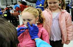 Enfermera escolar le administra la vacuna en atomizador nasal a una niña pequeña