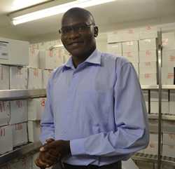 Kenyan medical epidemiologist Tamu Collins standing in a storage room filled with tetanus vaccine
