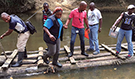 Liberian disease detective trainees carefully cross a river on a long raft to reach remote settlements