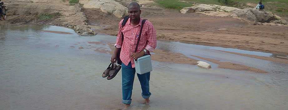 Nigeria FETP resident Dr. Wada Imam Bello carrying polio vaccine on foot across a river to reach 