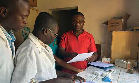 FETP resident Gauthier Mubenga reviewing data collection forms with laboratorians at the Yomou prefectural hospital in N’Zérékoré, Guinea