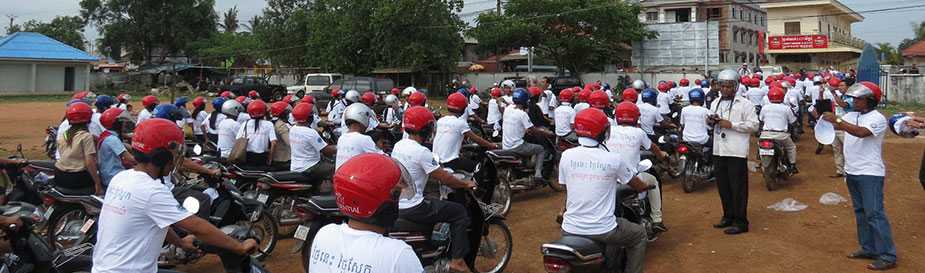 Cambodian motorcyclists, many in red helmets, learn how to ride safely