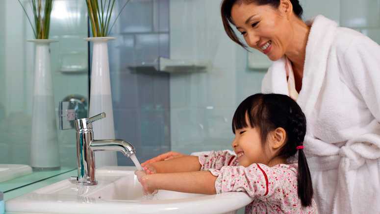 mother helping daughter wash her hands at sink