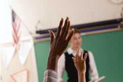 2 students raising their hands to answer the teacher's question in class