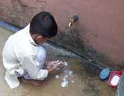 Child washing hands outside under a water spigot