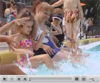 Image excerpt from the video showing a group of women, of various ages, splashing their feet in a pool.