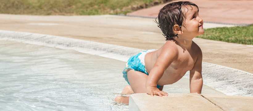 a toddler in a diaper crawling out of a swimming pool onto the deck