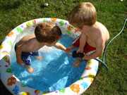Two boys filling a kiddie pool with water.
