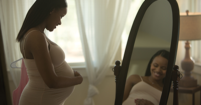Photo of a smiling pregnant woman looking at herself in the mirror