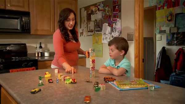 A woman stacking blocks with her young son while instructing him