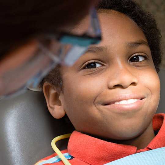 A young boy in dental chair smiling up at his dentist