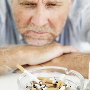 Photo: man staring at an ashtray with cigarette butts and a lit cigarette