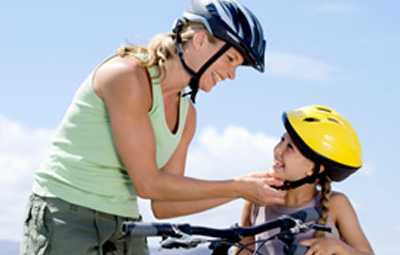 Photo: Mother placing a bicycle helmet on her daughter. 