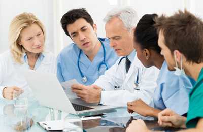Healthcare professionals sitting around a table looking at a document held by a doctor.