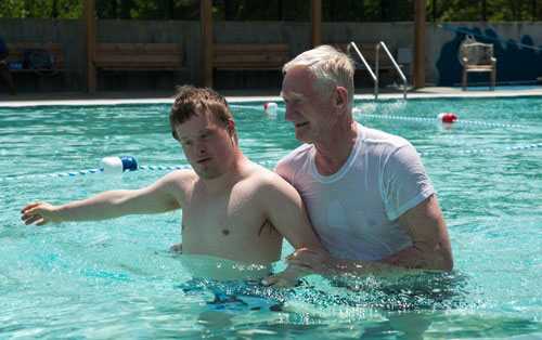 A disabled man in the pool with a caretaker. 