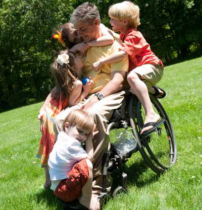 Niños abrazando a su papá que está en una silla de ruedas