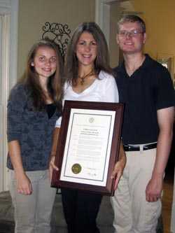 Sasha con su madre, Melissa, y su hermana, Nadia, sosteniendo una proclamación firmada por el Gobernador de Georgia en 2013 declarando el 9 de septiembre como Día de Concientización sobre el TEAH.