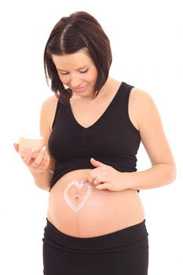 Pregnany woman making a heart on her stomach with lotion