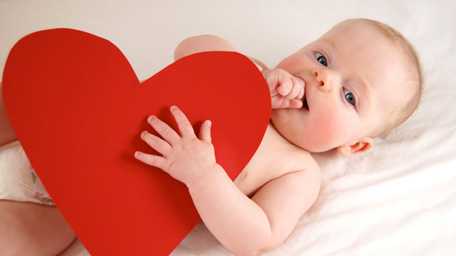 A newborn baby holding a red heart cutout