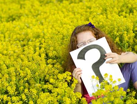 Girl in a meadow holding a sign with a question mark on it