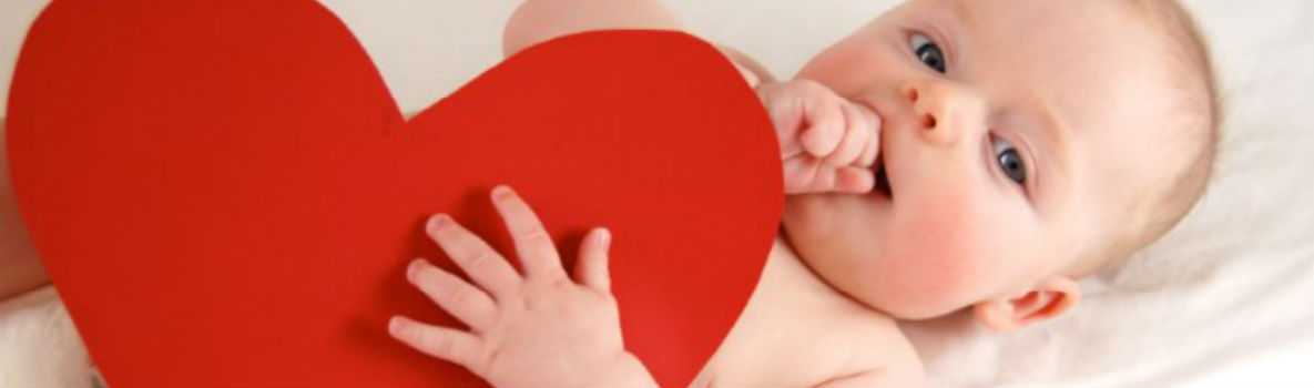 Baby lying on back holding a red heart cutout