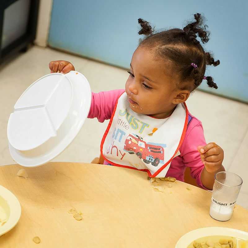 A young girl tips over her plate.